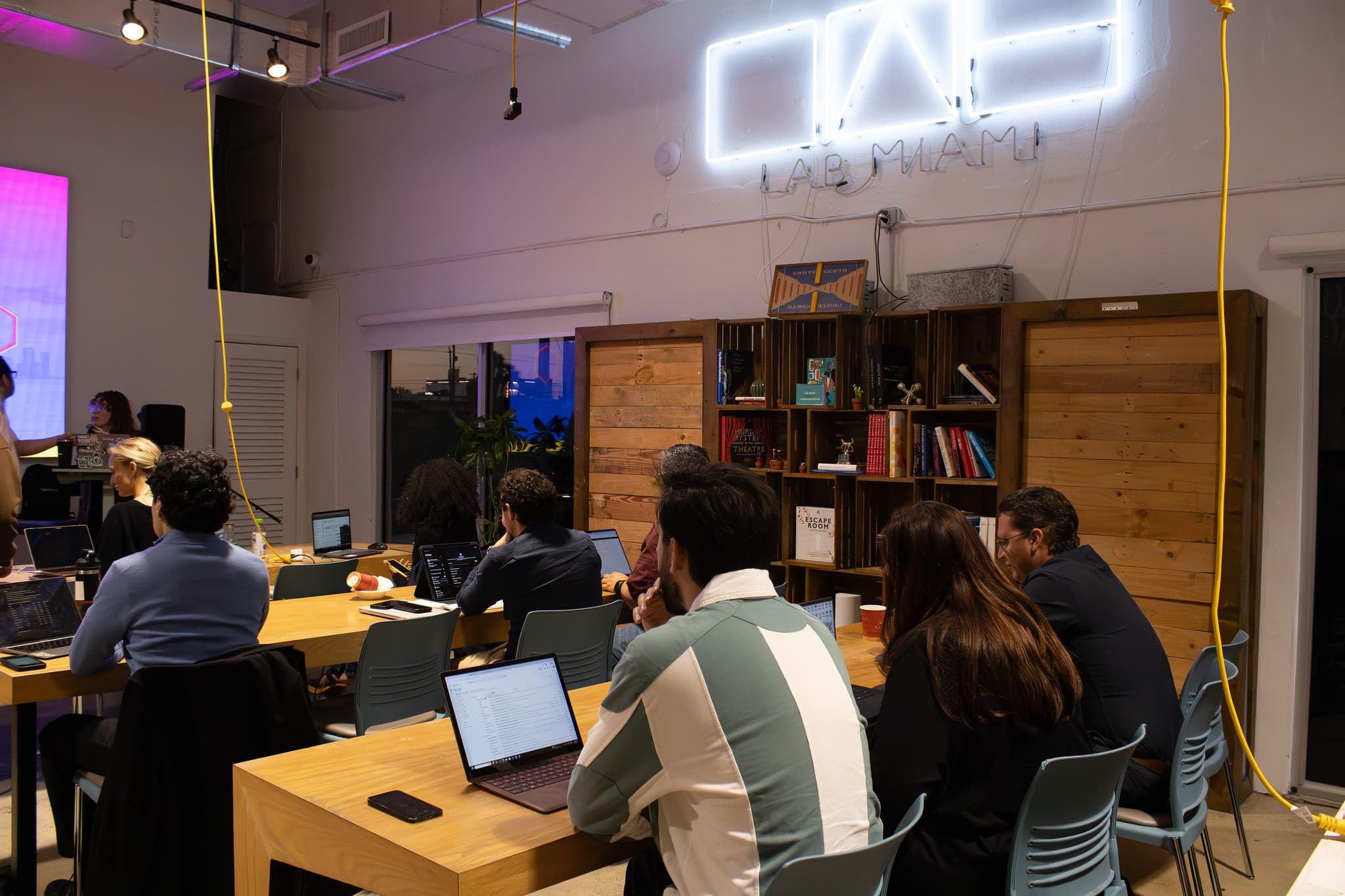 Builders working on laptops under The LAB Miami neon sign